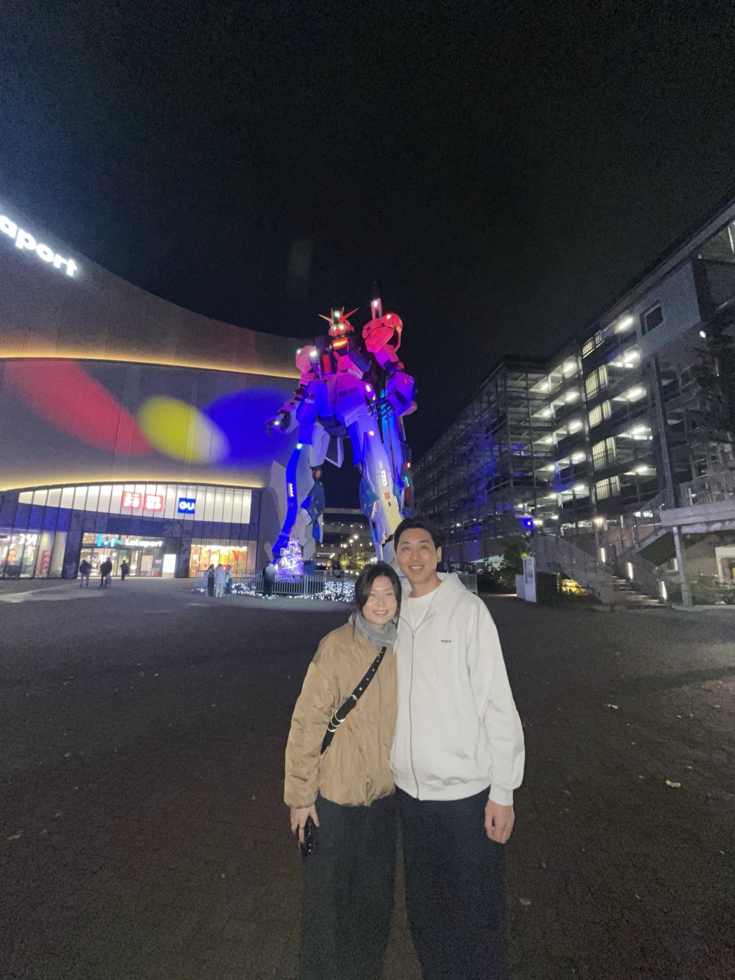Angela at night beside an illuminated Gundam statue